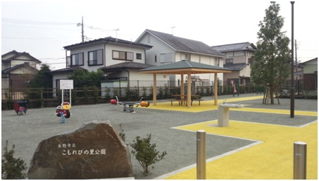 新しく整備された公園には、黄色い舗装が目立つ遊歩道、木製の四阿、石碑、そしてバネ付きの遊具がいくつか配置されている、こもれびの里公園の写真