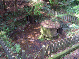 木製の杭と柵で囲まれた中にコンクリート製の円形の構造物がある現在の紀伊ノ守水源の様子の写真