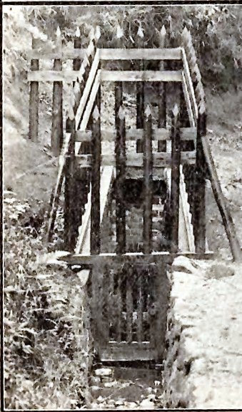 古い水路に、先が尖った木製の柵と鉄格子が設置されているロ号水源の様子を正面から撮影した白黒写真