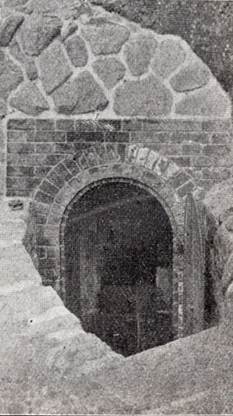 周囲を石で囲んだ丸いレンガ造りのトンネルの形をした入り口が特徴的な、ハ号水源を撮影した白黒写真