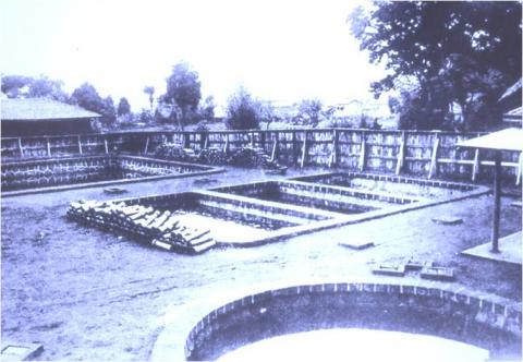 周囲を木々と板張りの壁に囲まれた敷地内に、四角や丸の形をした複数の貯水池がある曽屋水道を写した白黒写真