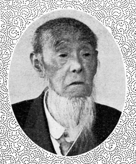 円形の枠の中に、ひげを生やした高齢の男性が写っている、梶山良助氏の白黒の肖像写真