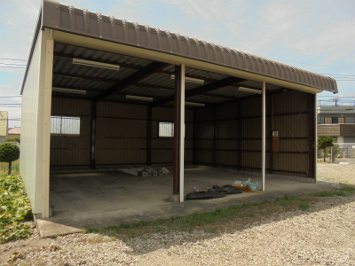 車庫のシャッターがすべて開き、内部のコンクリートの床に少量の資材が置かれている状態を斜めから捉えた写真