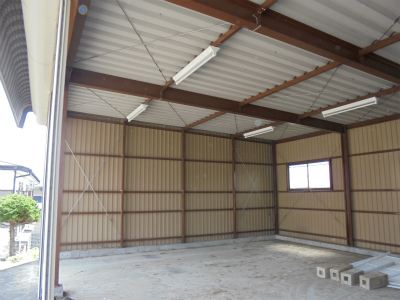 茶色い鉄骨とベージュ色の金属製の壁で構成され、コンクリートの床が広がり、天井に蛍光灯が取り付けられている車庫内部の様子の写真