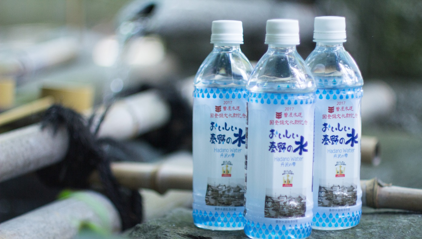 ぼかしのかかった竹筒や柄杓の横に、秦野市が「おいしい秦野の水」として販売している水玉模様の青いラベルのペットボトル3本が並んでいるイメージ写真