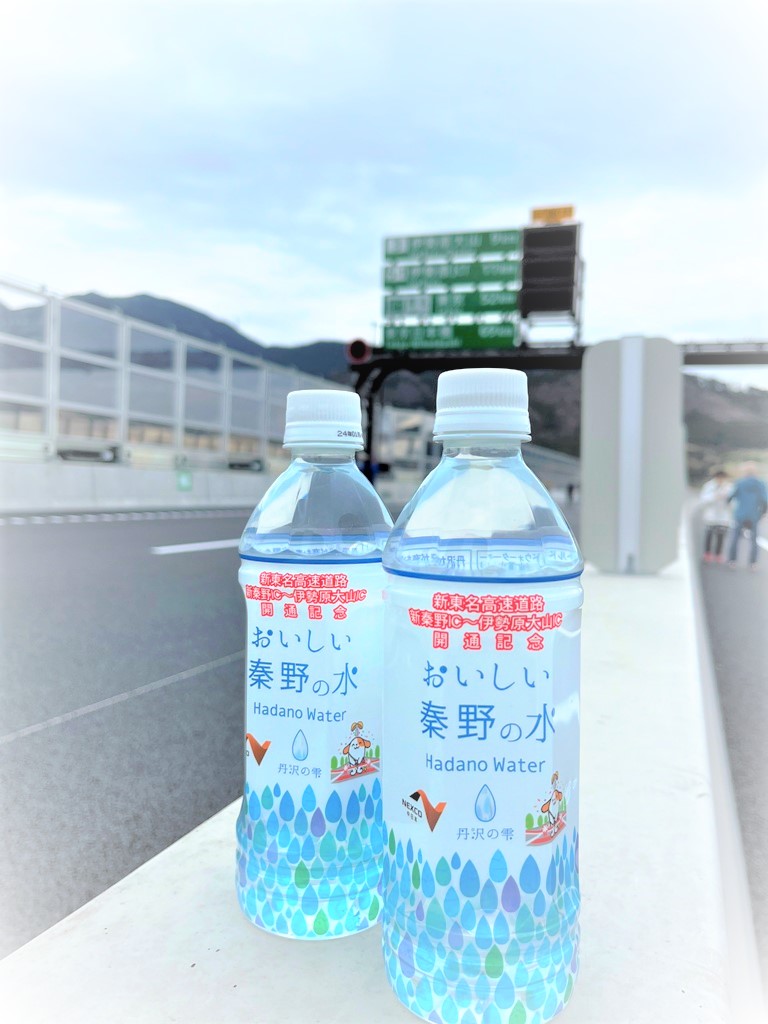 「おいしい秦野の水 」のラベルが貼られたペットボトル2本が、新東名高速道路のインターチェンジ付近の道路脇コンクリートの上に置かれている写真