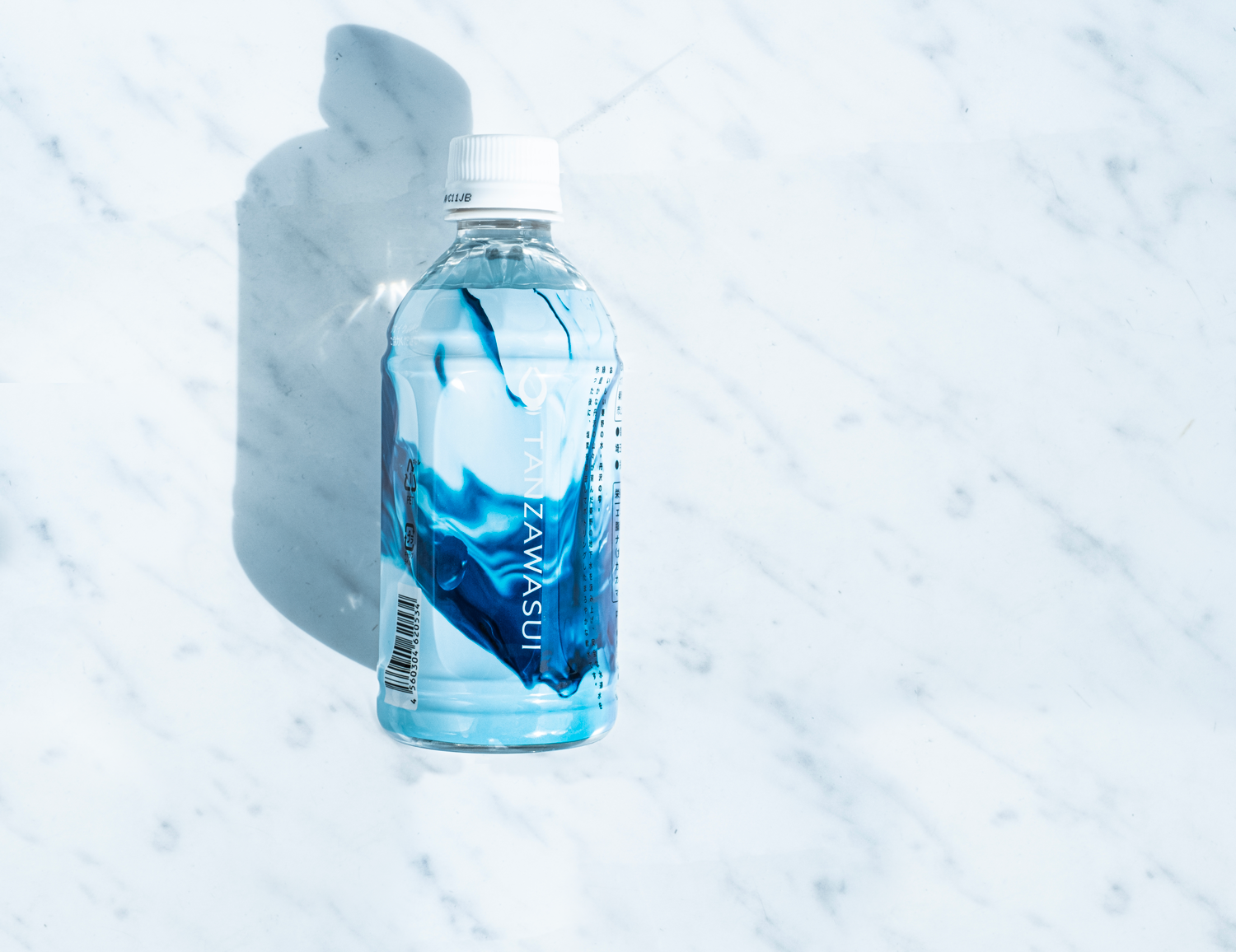 青い波のような模様がデザインされたラベルの透明なペットボトル入り「TANZAWASUI（丹沢水）」が置かれている商品写真