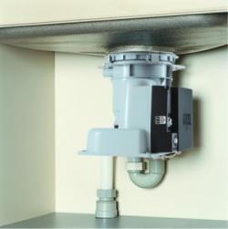 キッチンの流しの下に設置された、排水口から伸びる配管に接続された灰色と黒のコンパクトな電動ディスポーザー装置を、真下に近い角度から捉えた写真