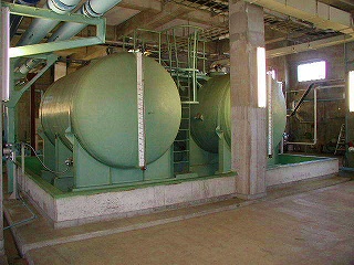 建物内部に設置された、水平に置かれた大きな緑色の円筒形タンクが2基あり、それぞれに目盛りのついた液面計がついている写真