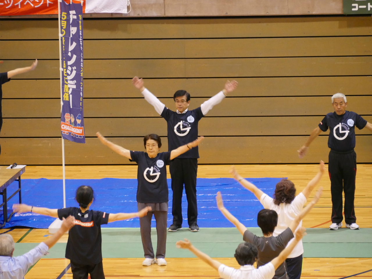 総合体育館オープニングセレモニーが行われており、同じロゴ入りTシャツを着た高橋市長と参加者が、腕を大きく広げ体操をしている様子の写真