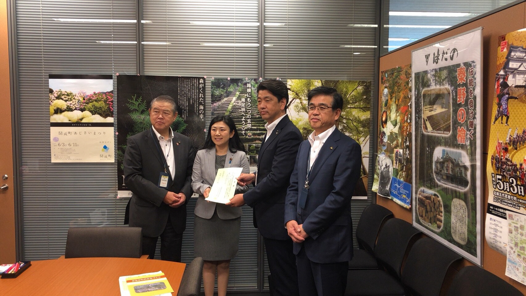 地域のポスターが貼られた応接室のような室内で、要望書を手に持つ関係者3人と高橋市長の写真