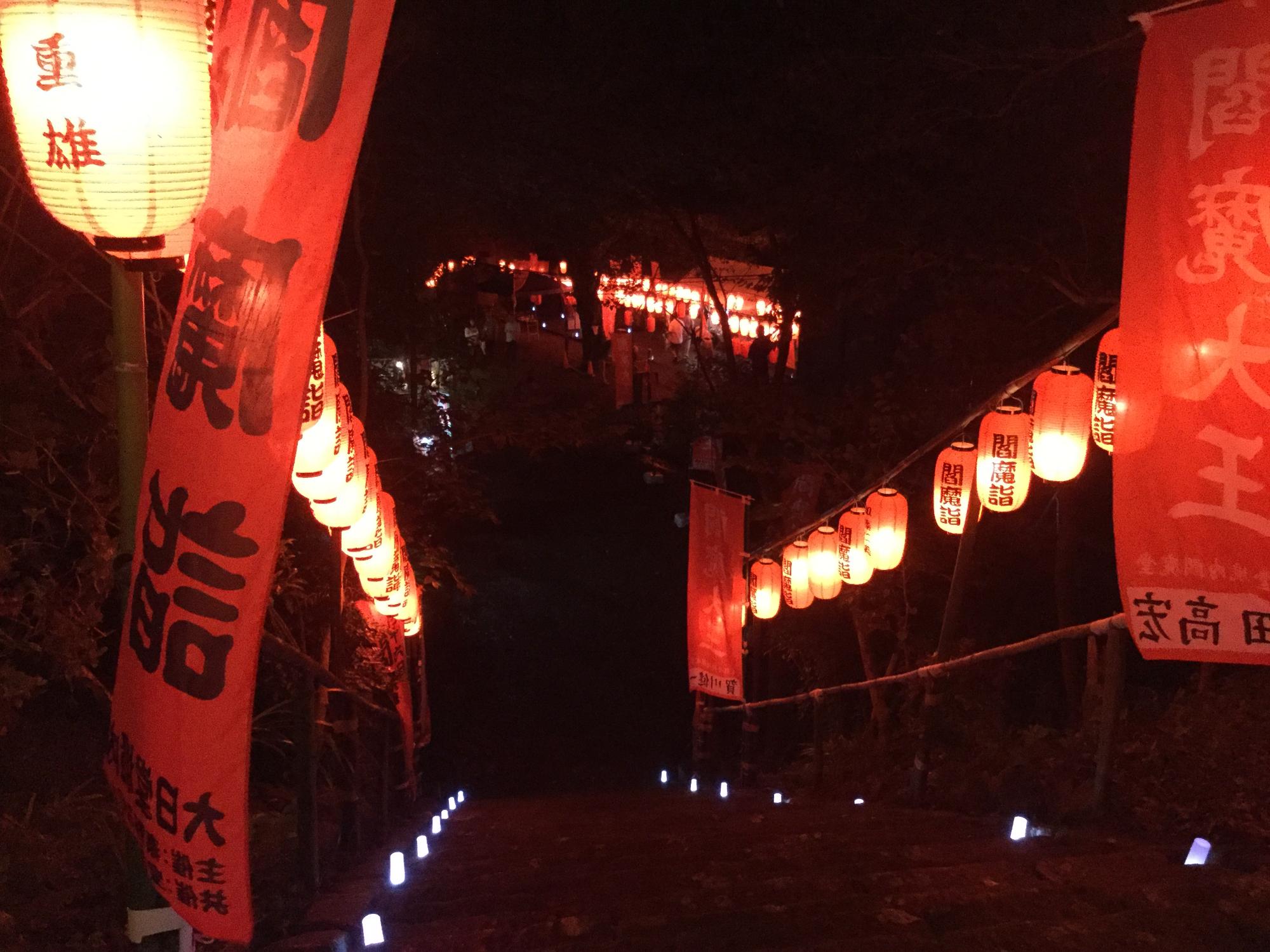 「閻魔詣」と書かれた旗や赤い提灯が階段に飾られ、赤く光る提灯の明かりが照らされる境内を階段上から見た写真