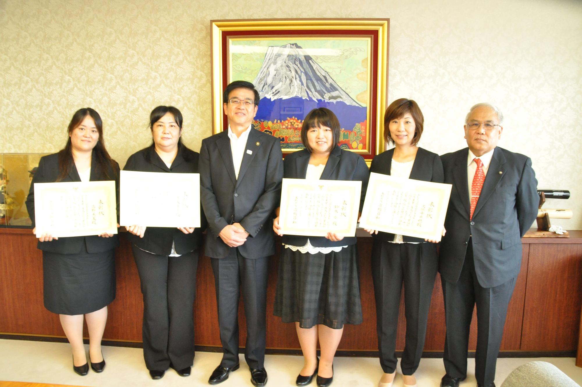 応接室のような室内に関係者と高橋市長が並び、そのうちの4人の女性が賞状を手に持ち、記念撮影を行っている写真