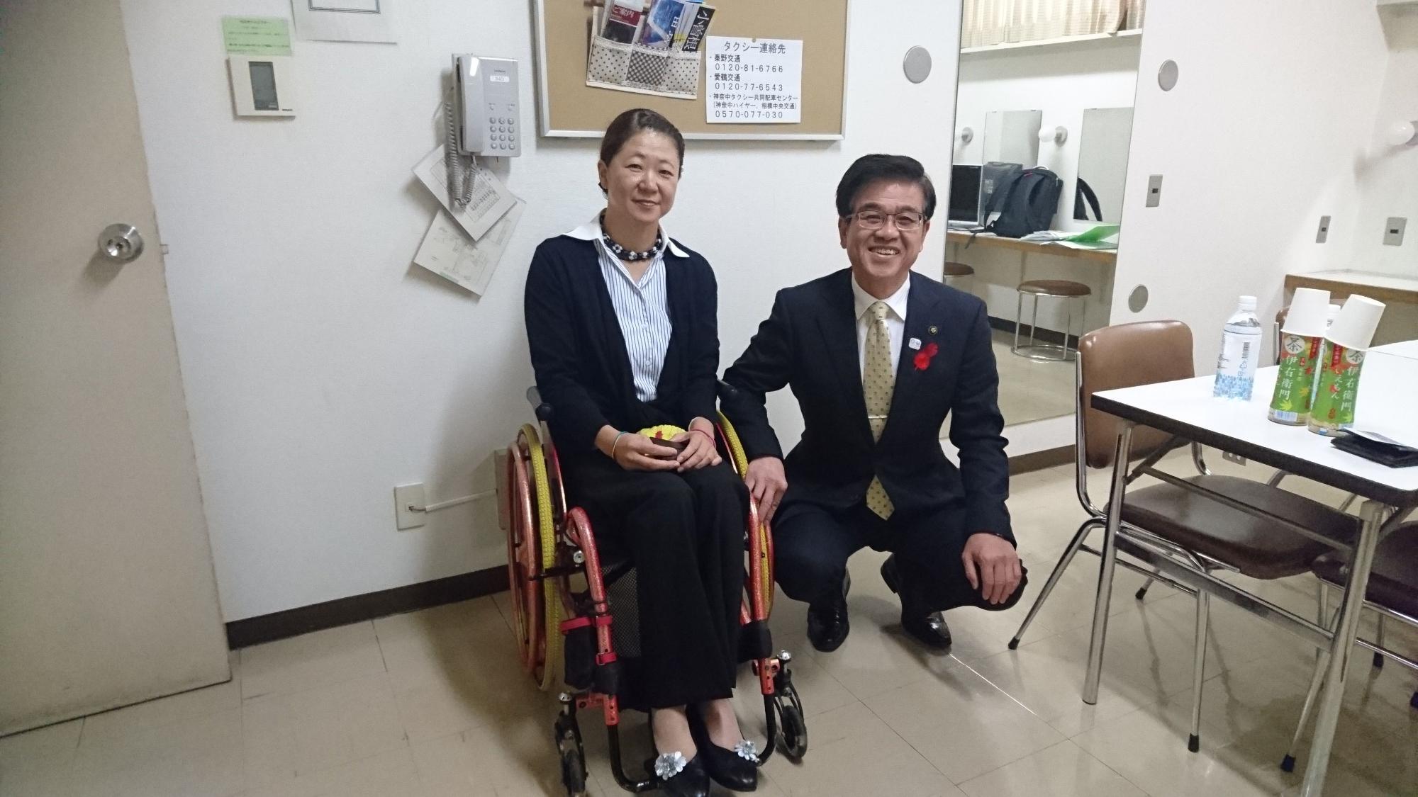 車椅子の成田真由美さんと、腰を下ろし、しゃがんでいる高橋市長が笑顔で記念撮影をしている写真