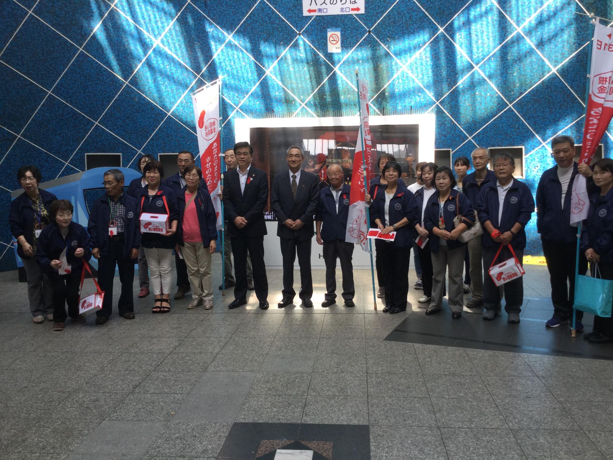 赤い羽根共同募金の旗や募金箱を手に持つ参加者が並んでおり、高橋市長と記念撮影している写真