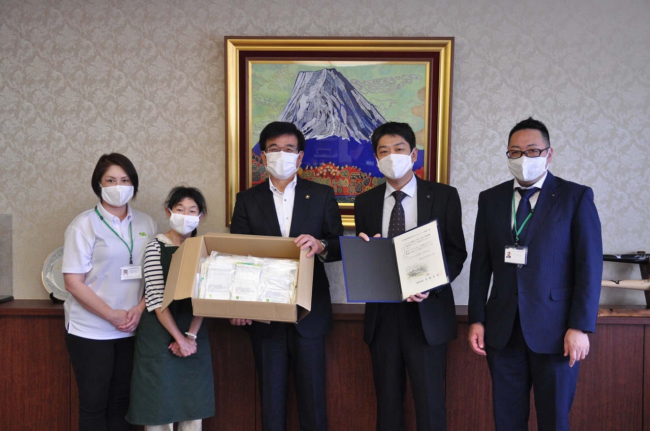 富士山の絵画が飾られた室内で、マスクを着用した市長を含む男女5人が立ち、中央のスーツ姿の市長が寄付された衛生用品の入った箱、隣の男性が感謝状を持って並んでいる写真