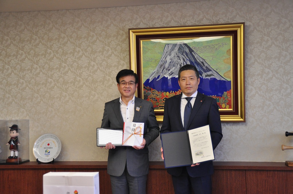 富士山の絵画が飾られている室内で、左側の市長が目録、右側のスーツ姿の男性が、感謝状を両手で持って笑顔で並んでいる写真