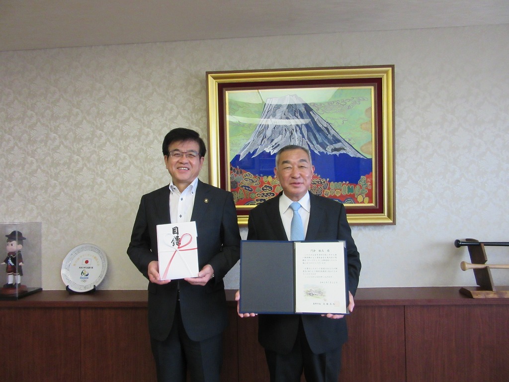 富士山の絵画が飾られた部屋で、市長は紅白の熨斗紙がかけられた目録、男性は感謝状のような書類を持ち、笑顔で並んでいる写真