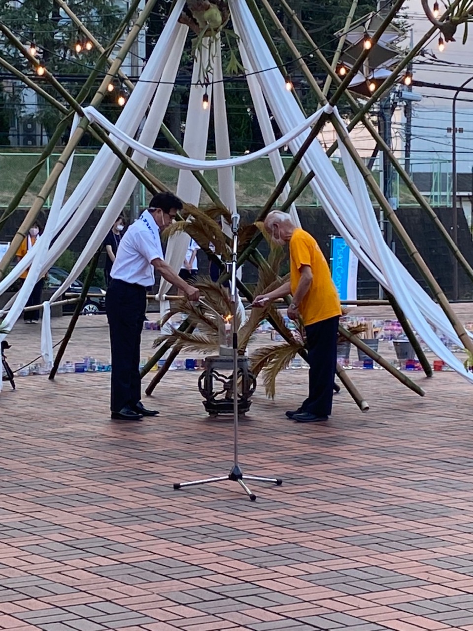 竹で組まれた骨組みに白い布が垂らされたモニュメントの下で、市長と男性でキャンドルに火を灯している写真