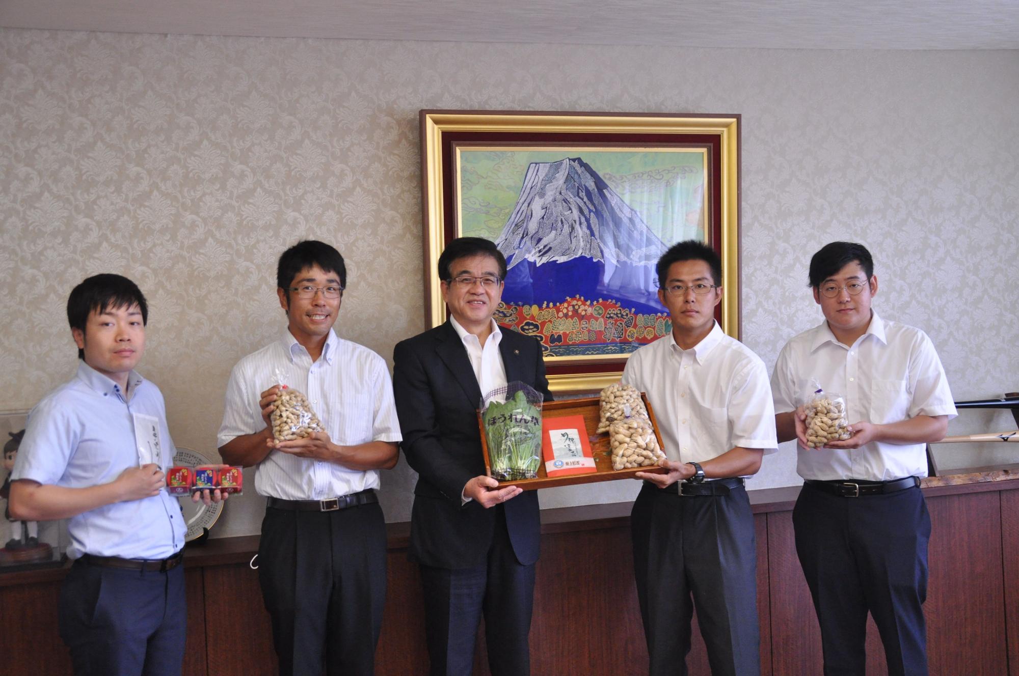 富士山の絵画が飾られた室内で、スーツ姿の市長が中央に立ち、4人の若者が袋入りの落花生を携え、落花生の寄贈をしている様子を写した写真