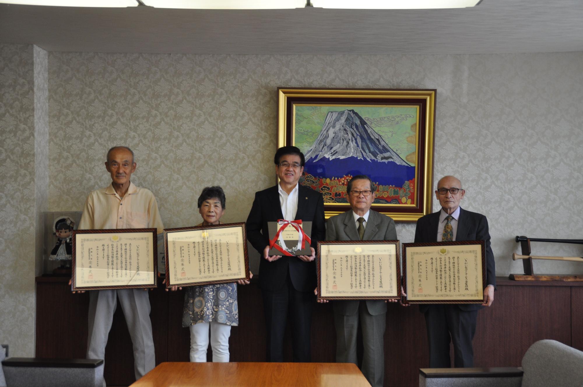 富士山の絵画が飾られた室内で、スーツ姿の市長が中央に盾士山の絵画が飾られた室内で、スーツ姿の市長が中央で表彰楯を持って立ち、4人の男女がそれぞれ賞状の額縁を持って並んでいる写真