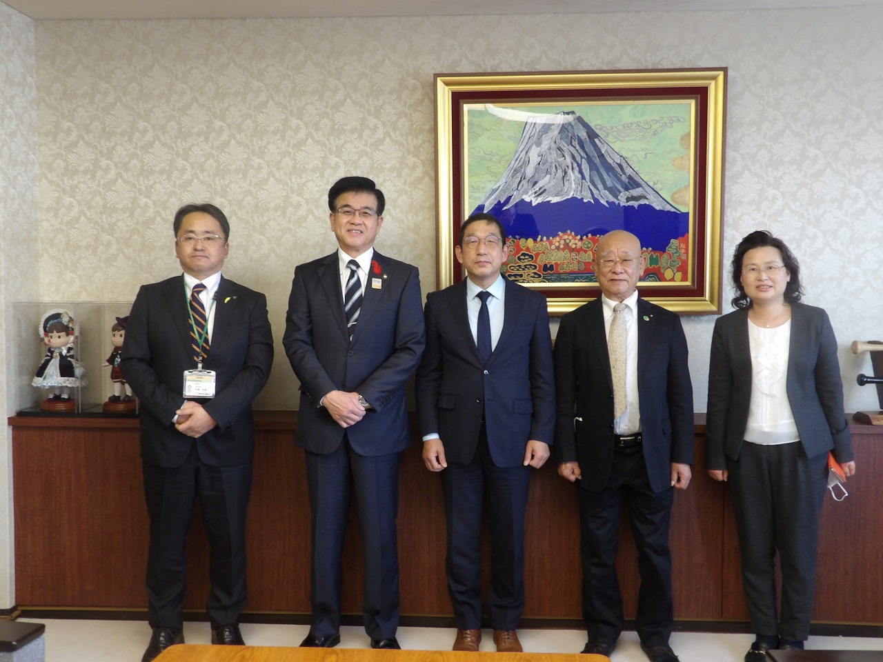 スーツ姿の男性4人と女性1人が背景には富士山の絵画が飾られている応接室でカメラに向かって並んでいる集合写真