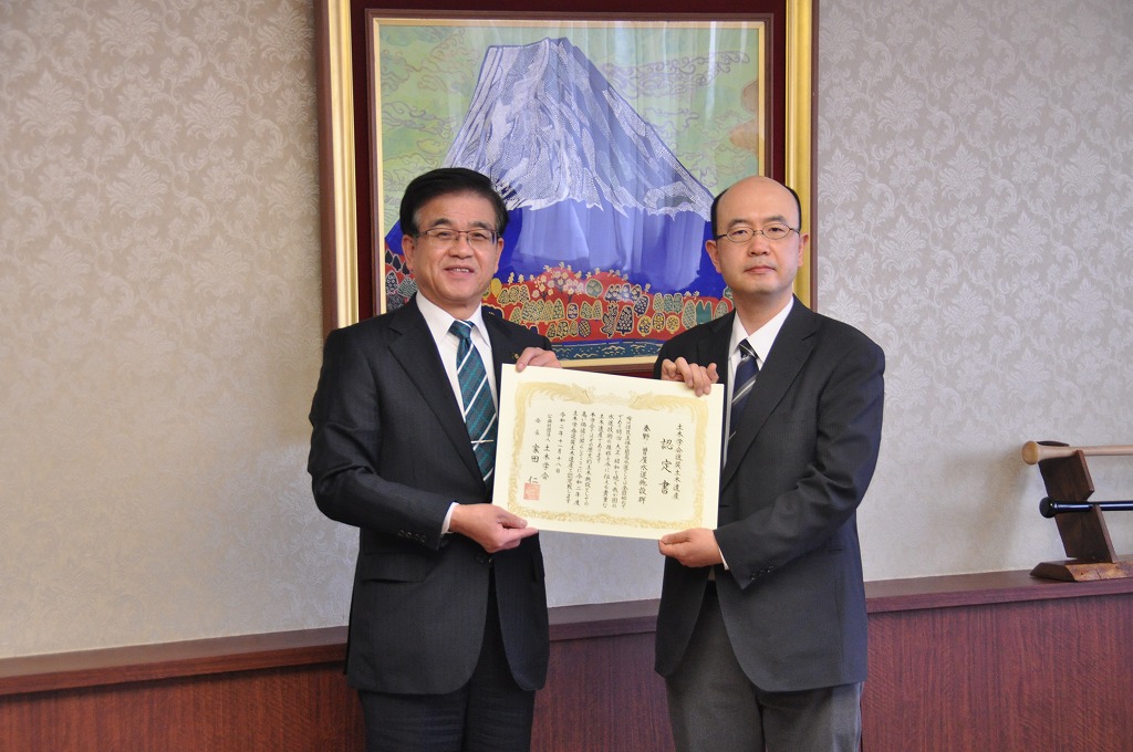 富士山の絵画が飾られた部屋で、スーツ姿の市長と男性で、認定書を持って並んで写っている写真