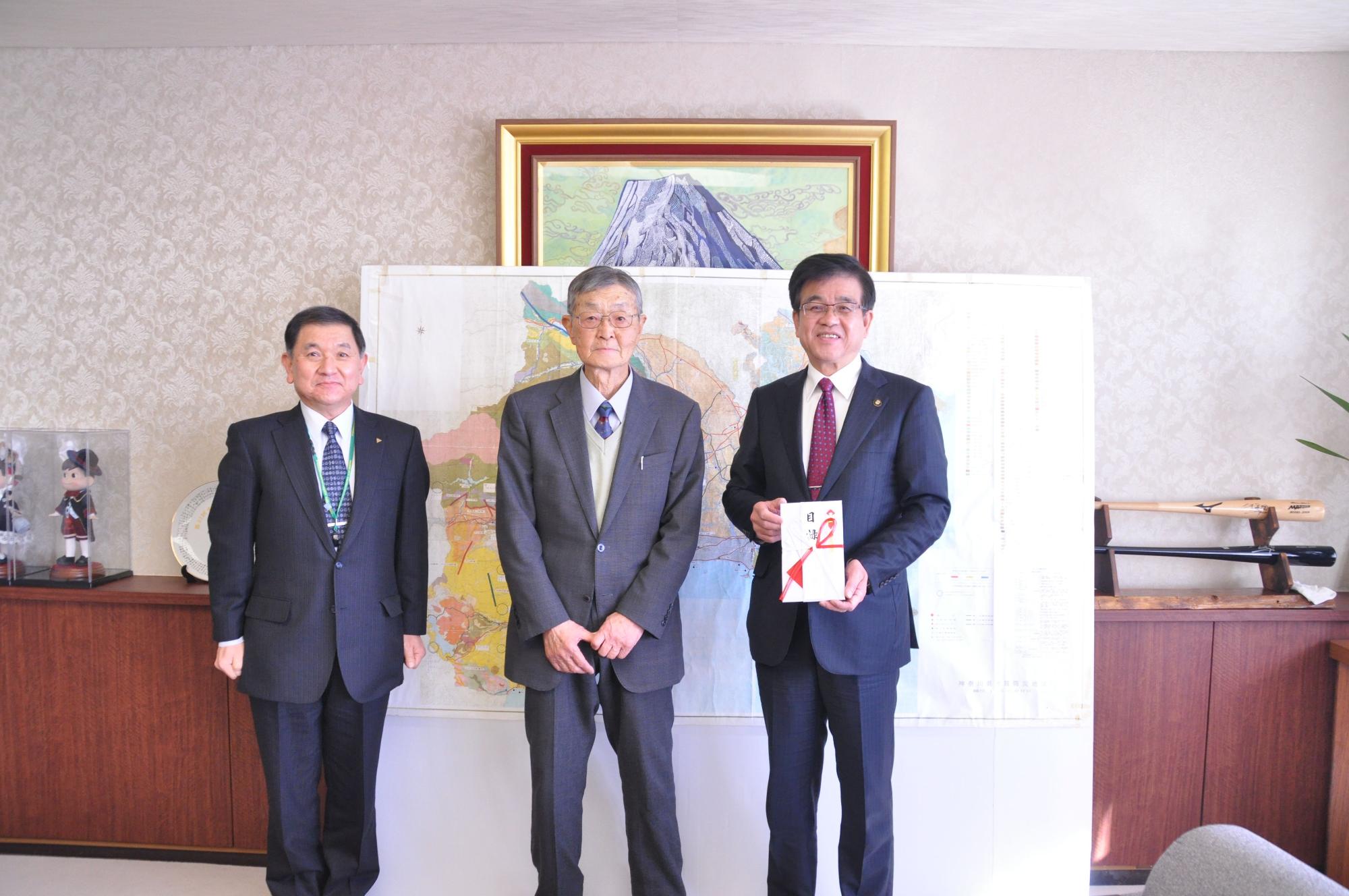 地震防災図の前でスーツ姿の男性2人と金封を手に持った市長が並び記念撮影している写真
