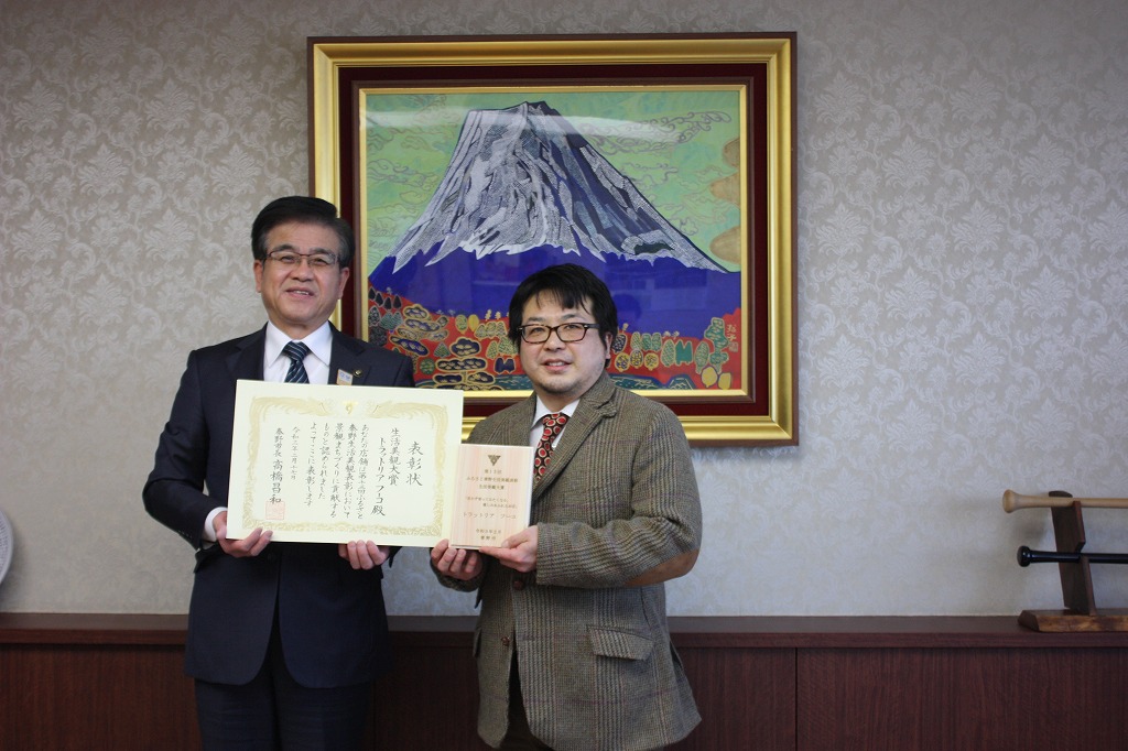 富士山の絵画が飾られた部屋で、市長と男性が賞状をそれぞれ持ち記念撮影している写真