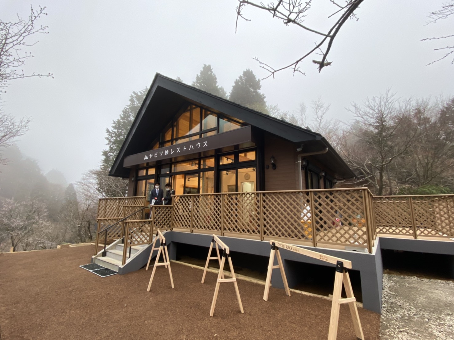 ヤビツ峠レストハウスと書かれたログハウス風の建物が建ち、木の柵で囲まれたテラスのあるレストハウスの外観写真