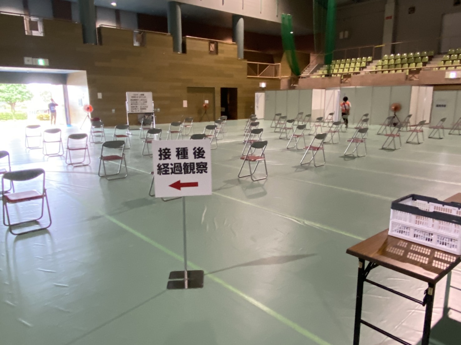 ワクチン接種後の経過観察エリアで、等間隔に配置された多くの椅子が並べられており、奥には受付のような場所が見える体育館内の写真