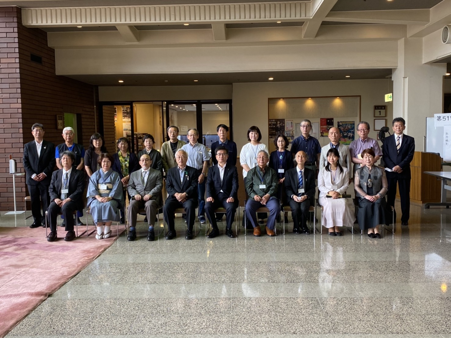 大勢の男女がフォーマルな服装で集まっており、中央には椅子に座った数名が並び、その両脇や後ろに立った人々がカメラに笑顔でポーズをとっている集合写真