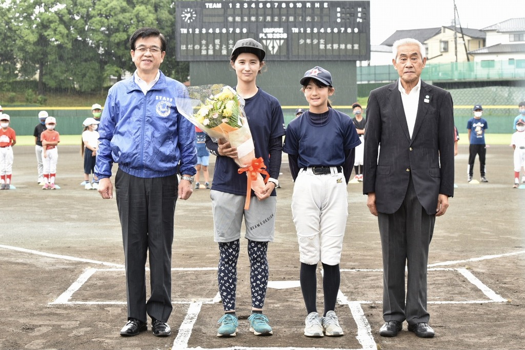 野球場を背景に、野球ユニフォーム姿で花束を持った加藤優さんとユニフォーム姿の女の子、スーツ姿の男性と青のジャンバーを着た市長が、ホームベース上で記念撮影している写真