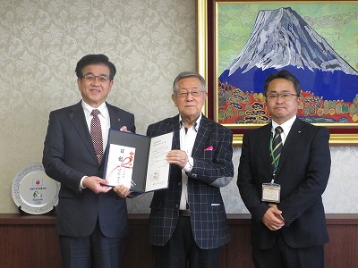富士山の絵画が飾られた部屋で、スーツ姿の市長と真ん中の男性で感謝状と目録が入ったファイルを持ち、3人並んでいる写真