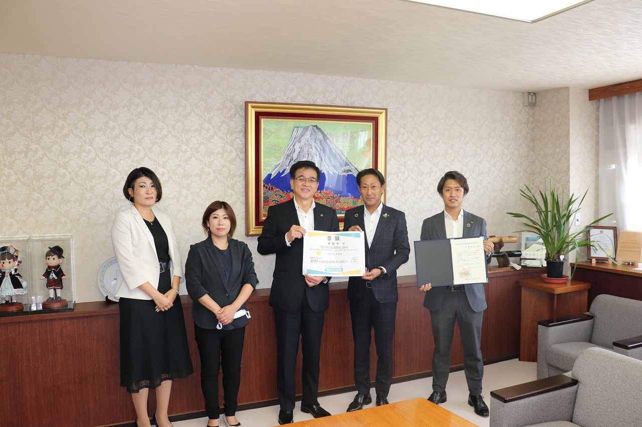 富士山の絵画を背景にした部屋で、市長と男性が目録を持ち、もう1人の男性が感謝状を持ち、市長の横に女性2人が並んだ記念写真