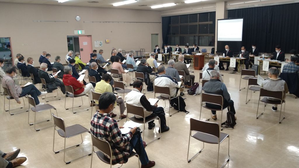 等間隔に並べられた椅子に座っている参加者たちが、室内前方の席に座っている方の話を聞いている懇談会の様子を遠景から撮影した写真