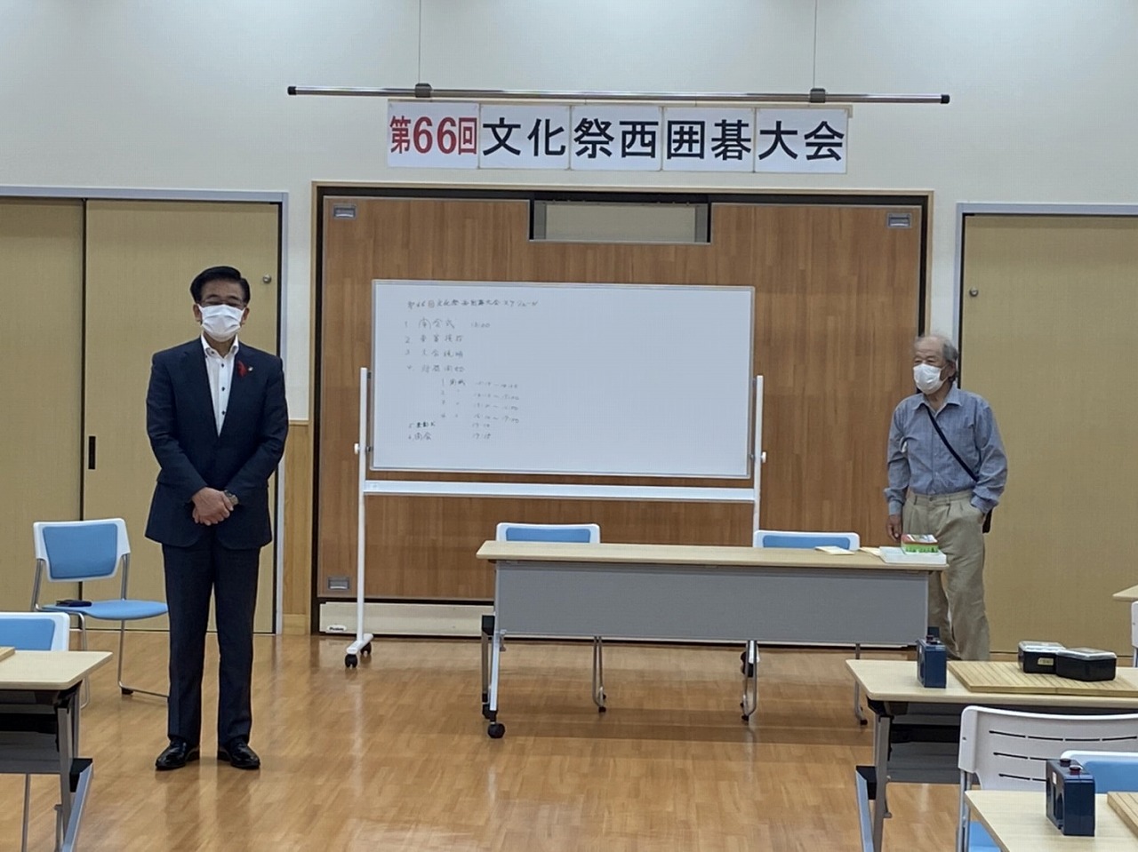 「第66回文化祭西囲碁大会」と書かれた紙が吊るされた室内の前方で、高橋市長が両手を前で組んで立ち、話をしている様子の写真