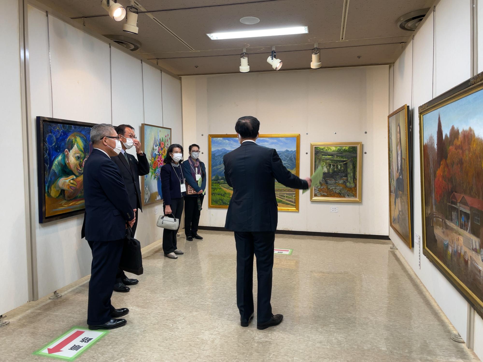 美術館の展示室でスーツ姿の高橋市長と他4人の男女がが風景画や人物画を鑑賞している様子の写真