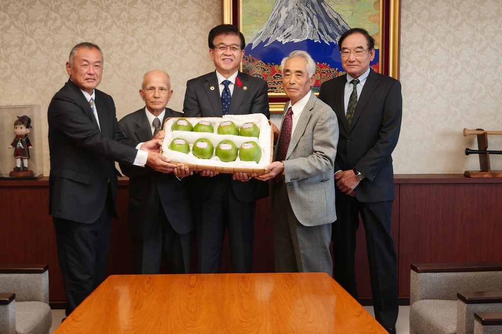 高橋市長を中心に3名の方と贈呈された青パパイヤを持ち記念撮影が行われている写真