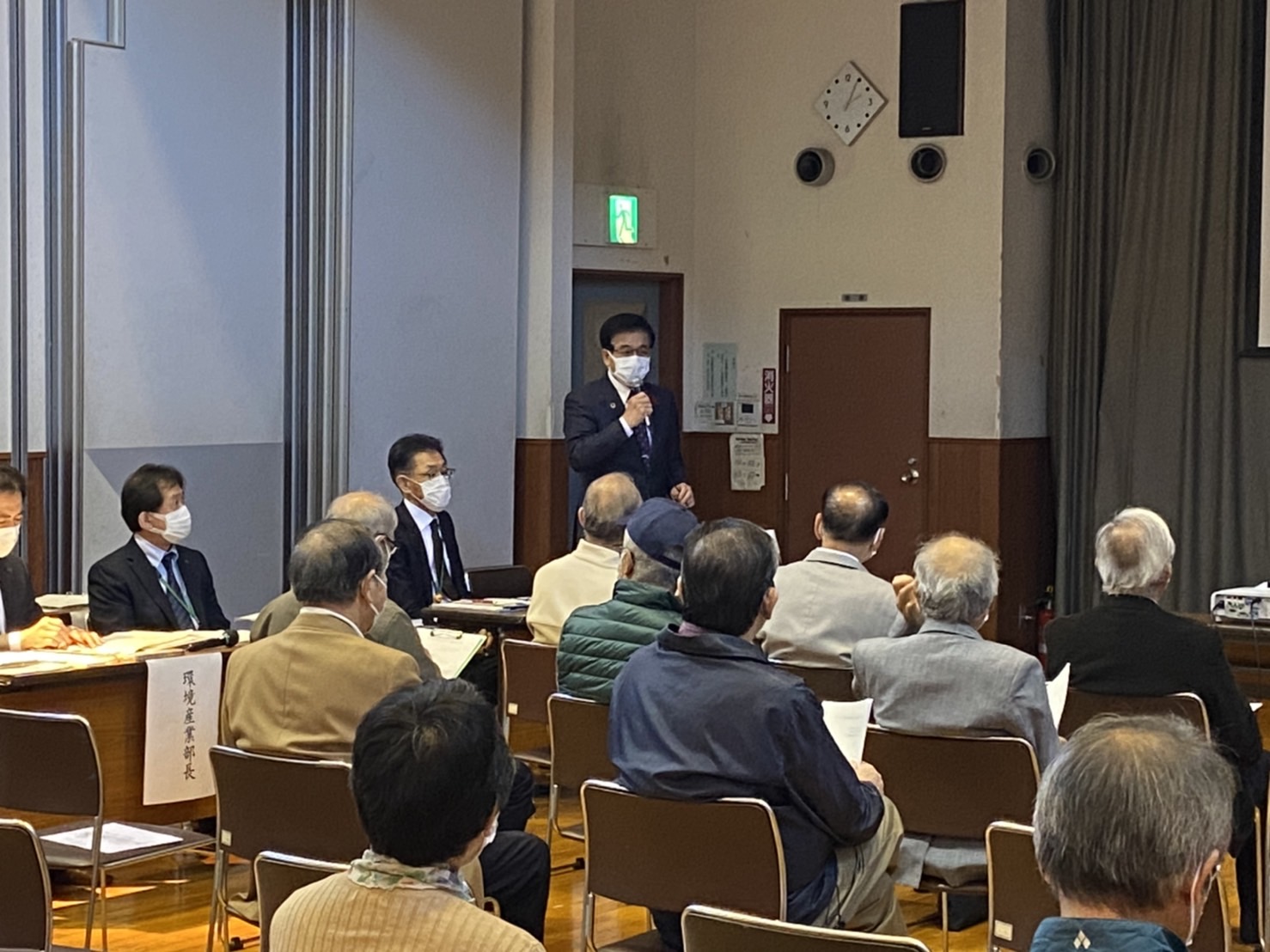 椅子に座る多くの参加者の前で、スーツ姿の高橋市長ががマイクを片手に話している鶴巻地区での市政懇談会の写真