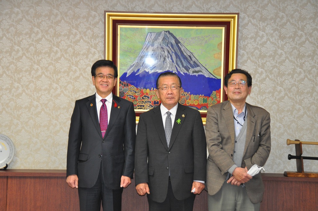 額縁に入った富士山の絵を背景に、スーツを着用した高橋市長、千葉県八街市北村市長、千葉大学斎藤名誉教授が並んで記念撮影を行っている写真