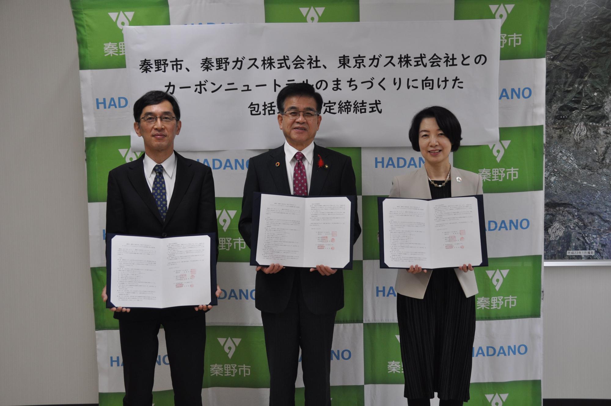 秦野市のバックパネルの前で高橋市長が秦野ガス株式会社の方、東京ガス株式会社方と一緒にそれぞれ協定書を広げてカメラに向かって立ち記念撮影をしている写真