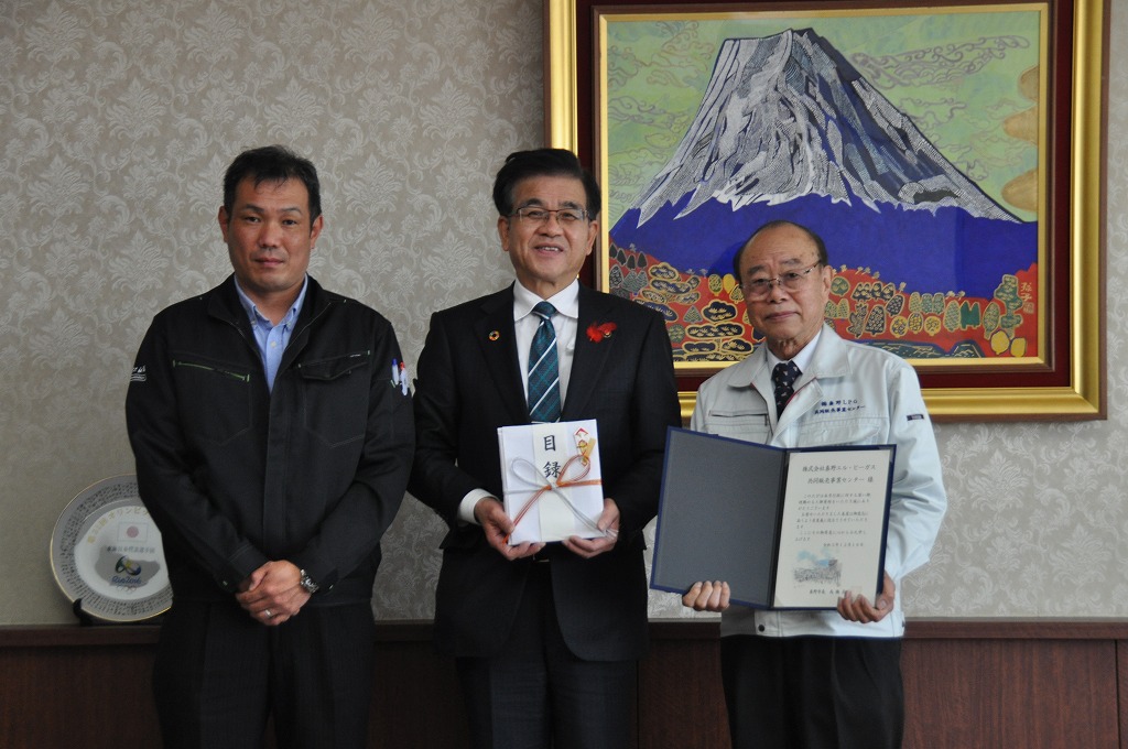 目録を持った高橋市長を中心に作業着姿の男性2名が並んで立ち、記念撮影をしている写真