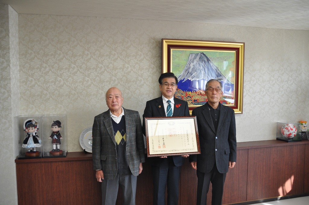 中央に額縁に入った賞状を持った高橋市長、両脇に羽根・菩提友愛チームの男性2名が立ち記念撮影をしている写真