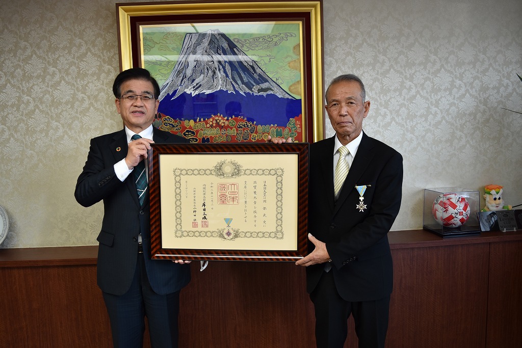 高橋市長と岡部武史さんが額縁に入った表彰状を一緒に持ち記念撮影をしている写真