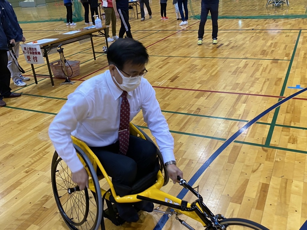 前方に車輪が1つ、後方に車輪が2つあるレース用車いすに乗っている高橋市長の写真