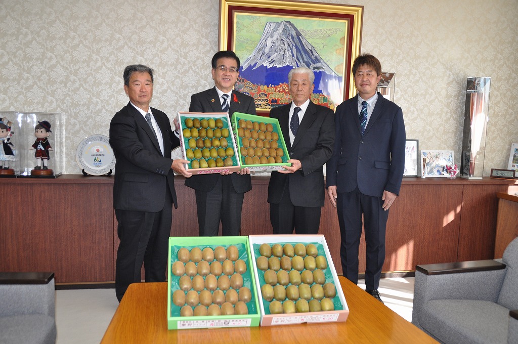 たくさんのキウイフルーツが入った箱が置かれたテーブルを前にして、高橋市長とスーツ姿の男性2名が一緒にキウイの箱持ち、その横にスーツ姿の男性1名が並んで立っている写真