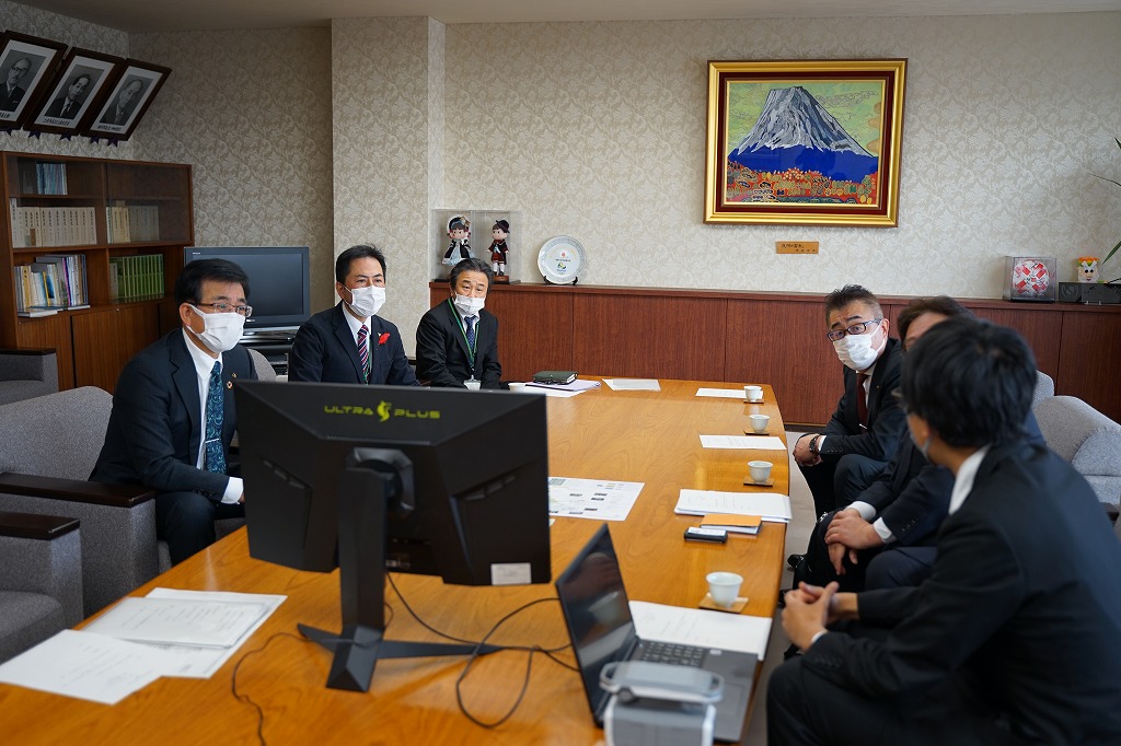 モニターやパソコン、資料が置かれた大きなテーブルを囲んで高橋市長や関係者などが話し合いをしている様子の写真
