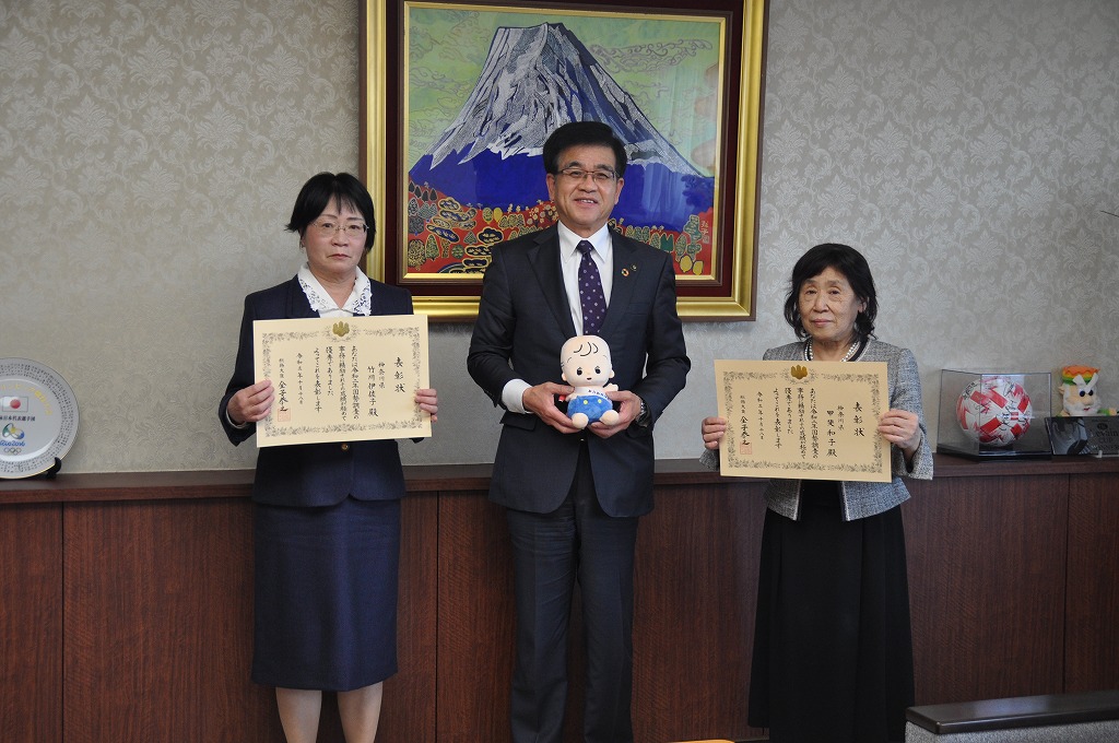 赤ちゃんの人形を持って立っている市長の両側に表彰状を持った女性2人が立ち、記念撮影をしている写真