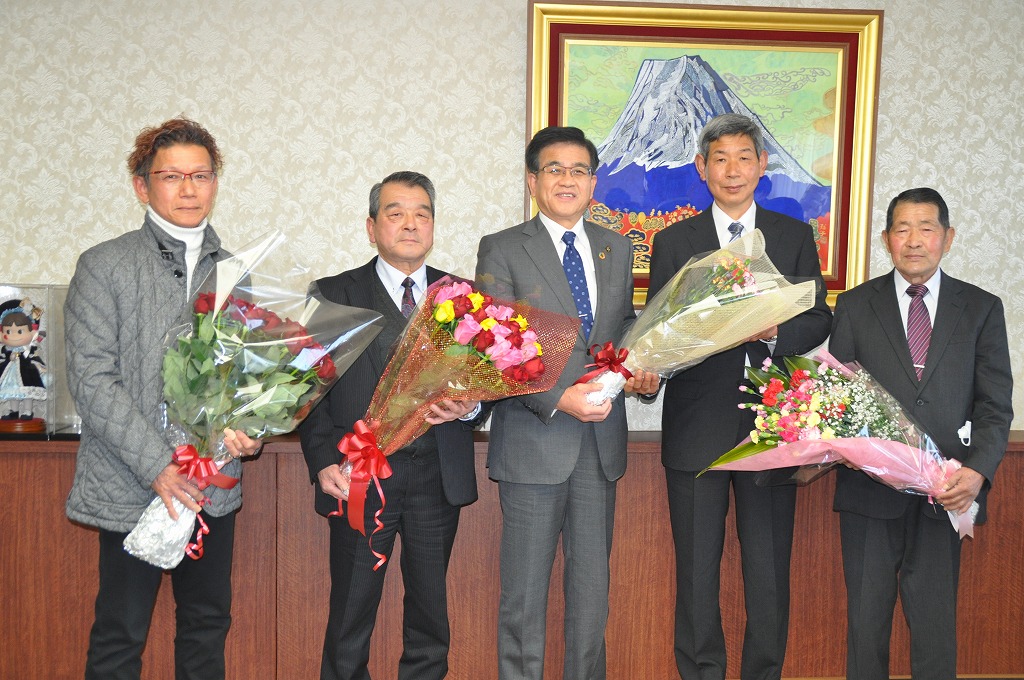 富士山の絵画が飾られた部屋で、市長を中央にしてスーツ姿やカジュアルな服装をした5人の男性が、それぞれ花束を持って立っている写真